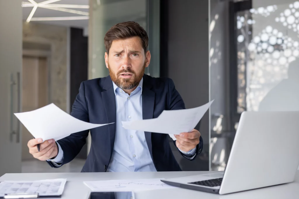 Worried man in a suit holding papers at his desk, reflecting stress over deciding between Chapter 7 and Chapter 13 bankruptcy options.