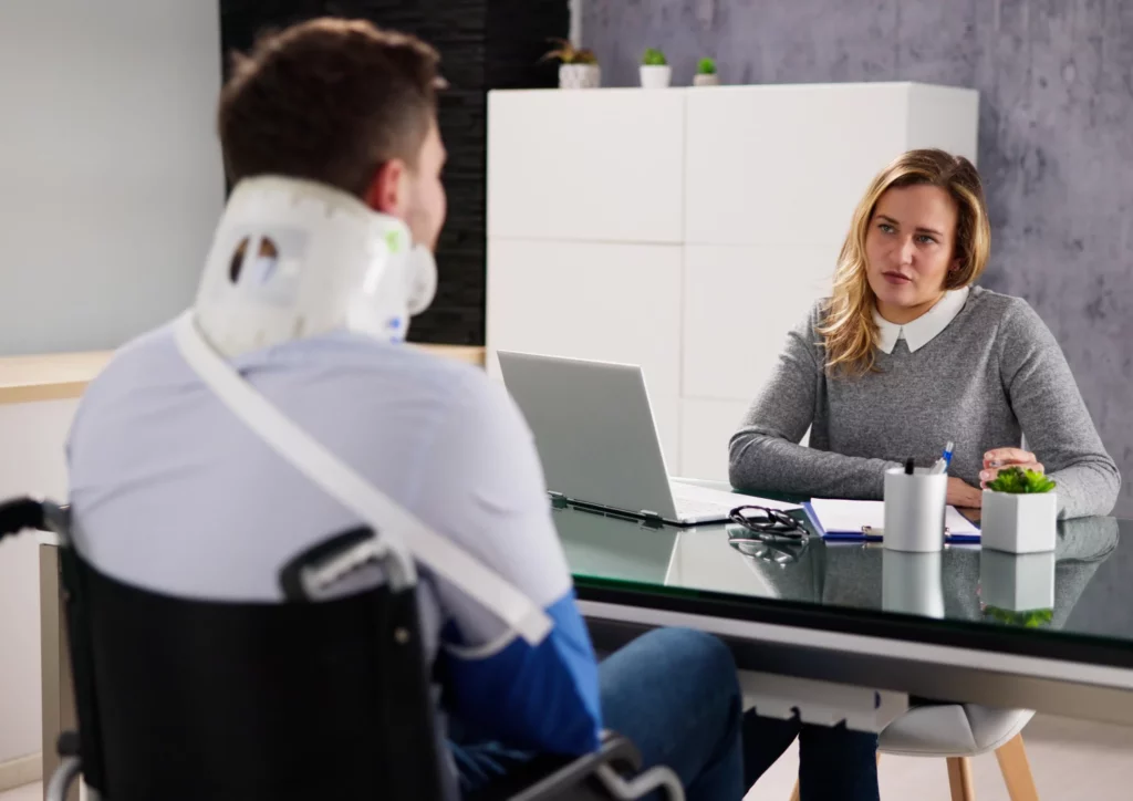 Personal injury lawyer meeting with an injured veteran in a wheelchair wearing a neck brace and arm sling.