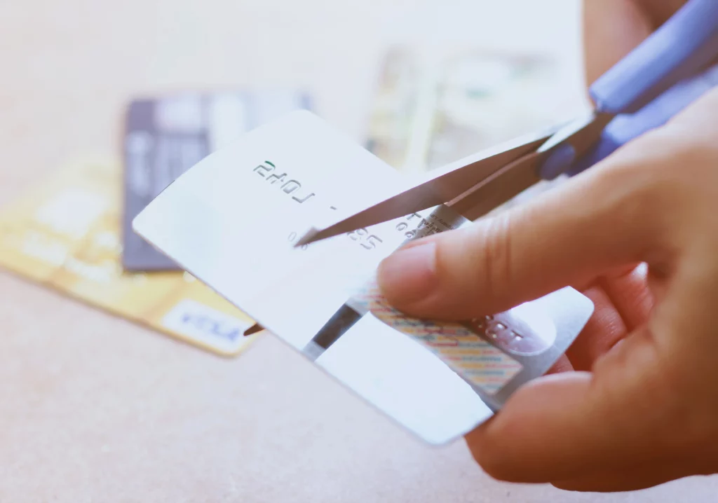Person cutting silver credit card in half with scissors on table with blurred credit cards