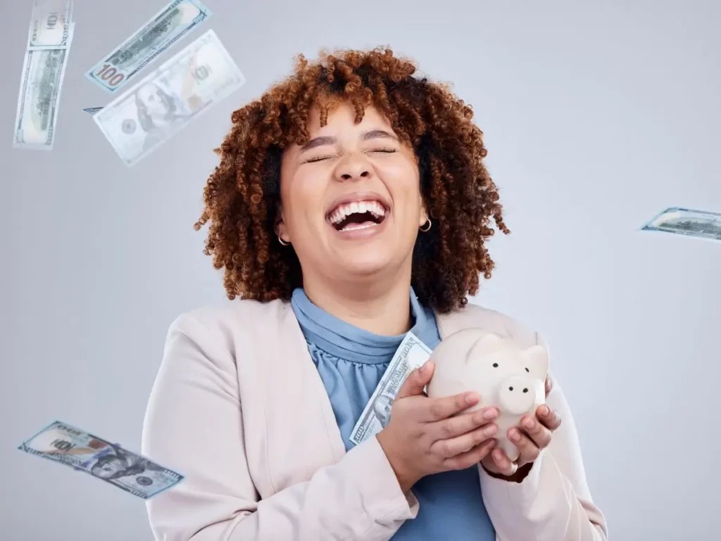 Happy woman holding a piggy bank with dollar bills falling around her, symbolizing financial relief and freedom after bankruptcy.