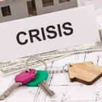House keys, cash, and a model home beside a sign reading ‘Crisis,’ symbolizing financial trouble and business bankruptcy concerns.