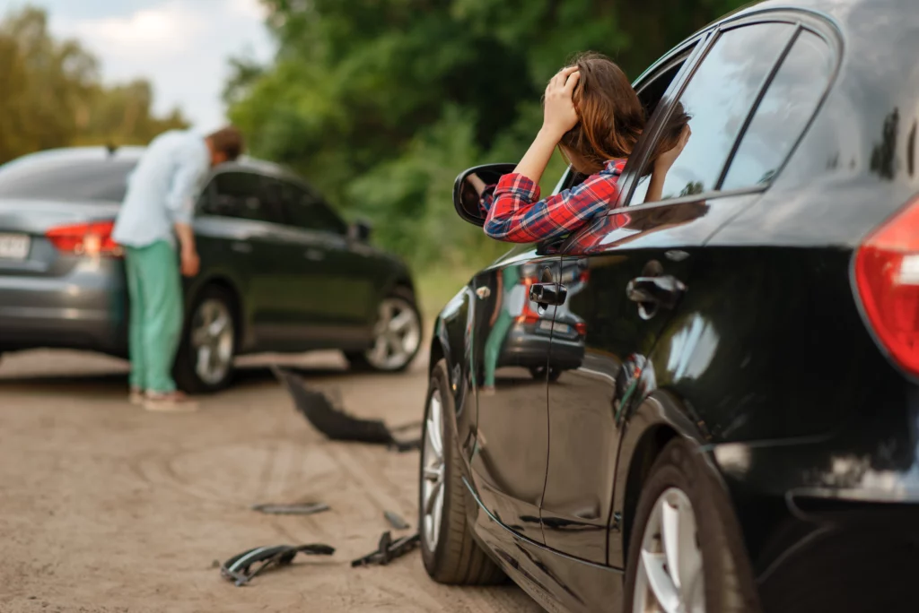 Distressed woman sitting in car after crash while person inspects damage between two vehicles on road, illustrating a minor car accident in Kentucky.